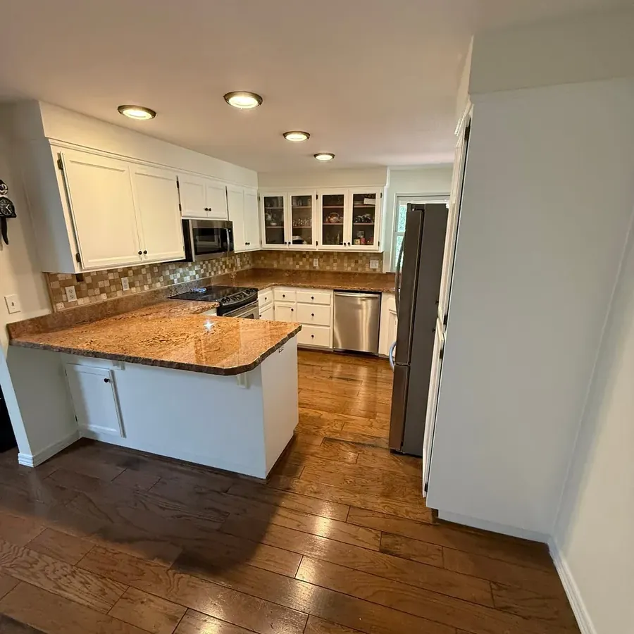 A kitchen with its cabinets refinished white, granite counters and a hardwood floor