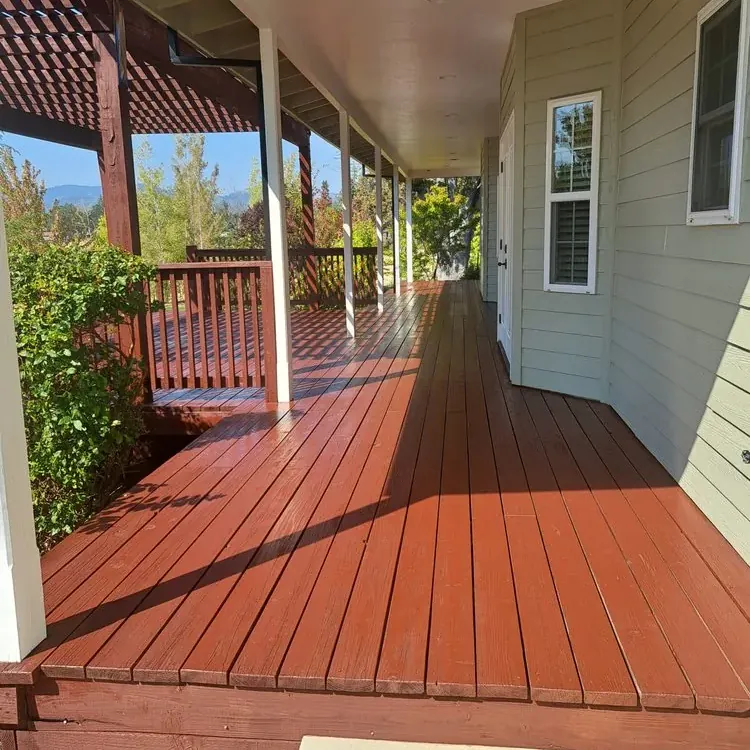 A long wraparound porch deck freshly stained red-brown along a sage green house