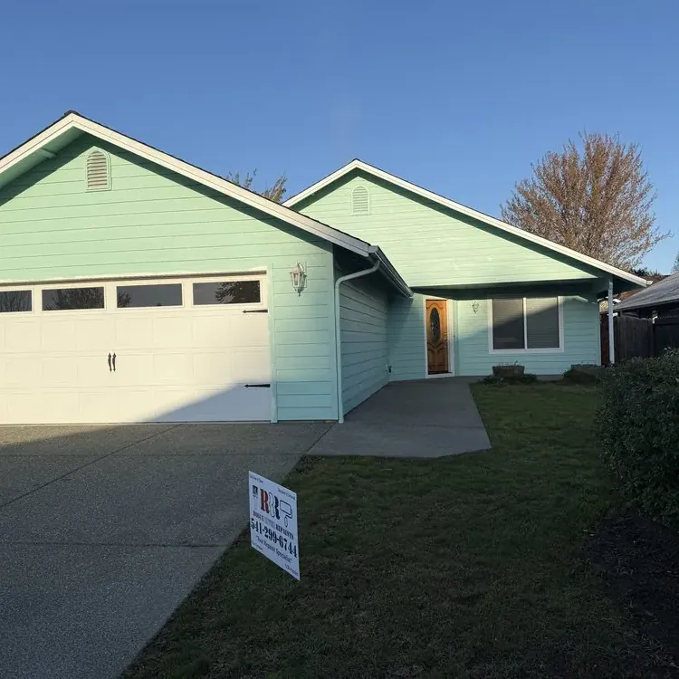 A single-story house repainted mint green, with a Rogue River Repaints yard sign on the lawn