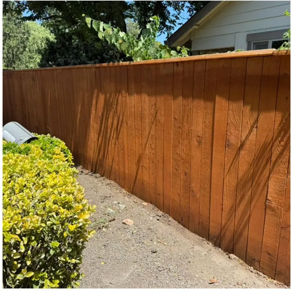 A long wood fence after power washing and sealing, stained a warm brown