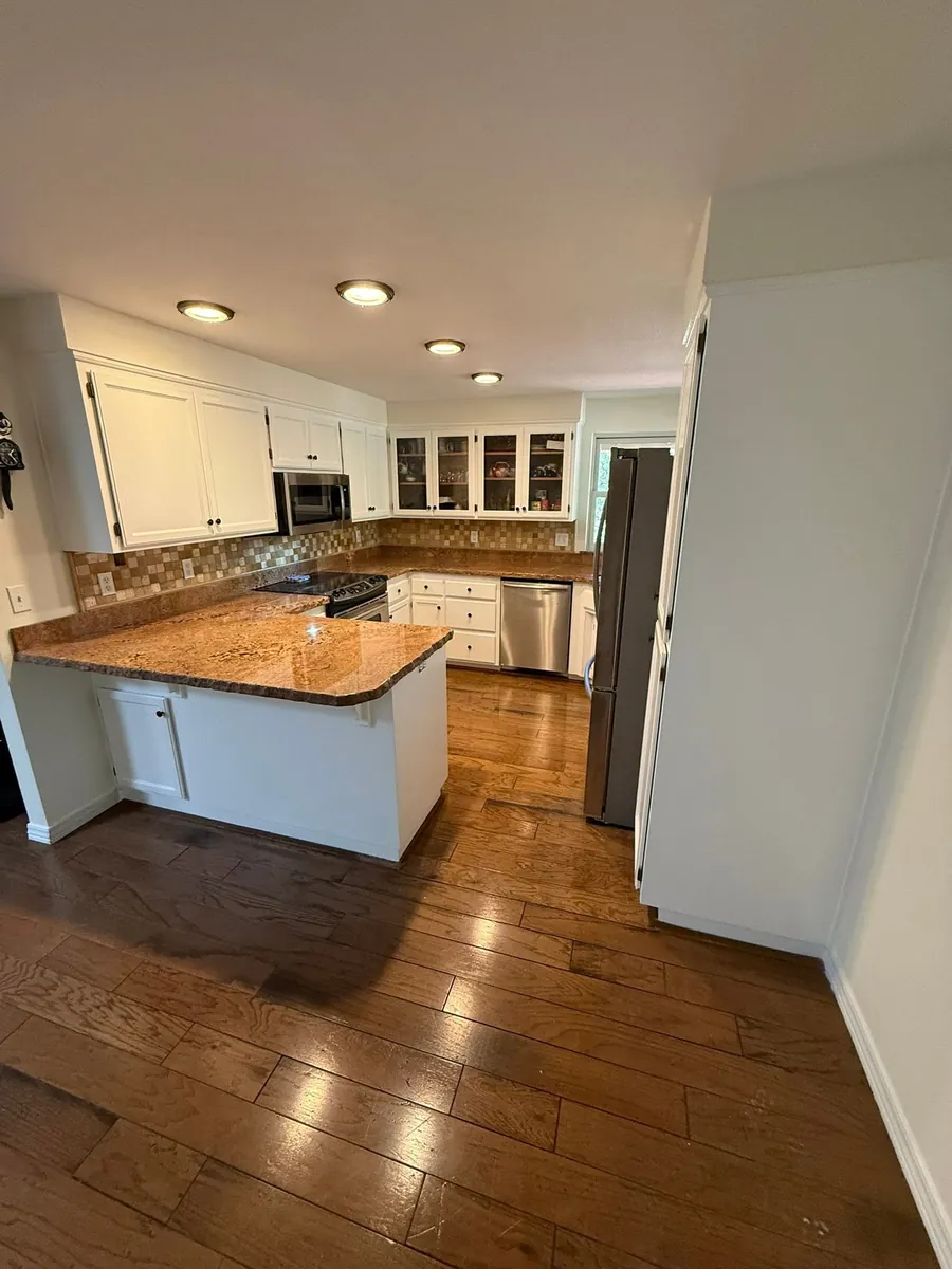 A kitchen with its oak cabinets refinished white, granite counters and a hardwood floor